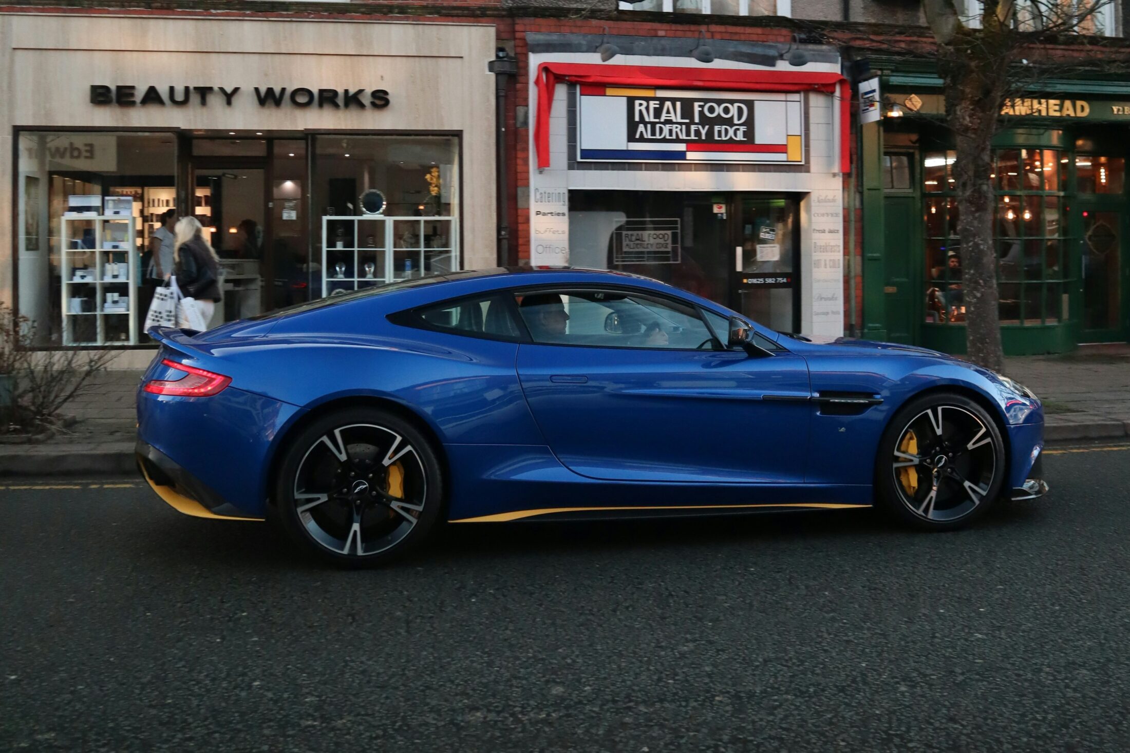 Aston Martin Vanquish S bleue dans une rue commerçante