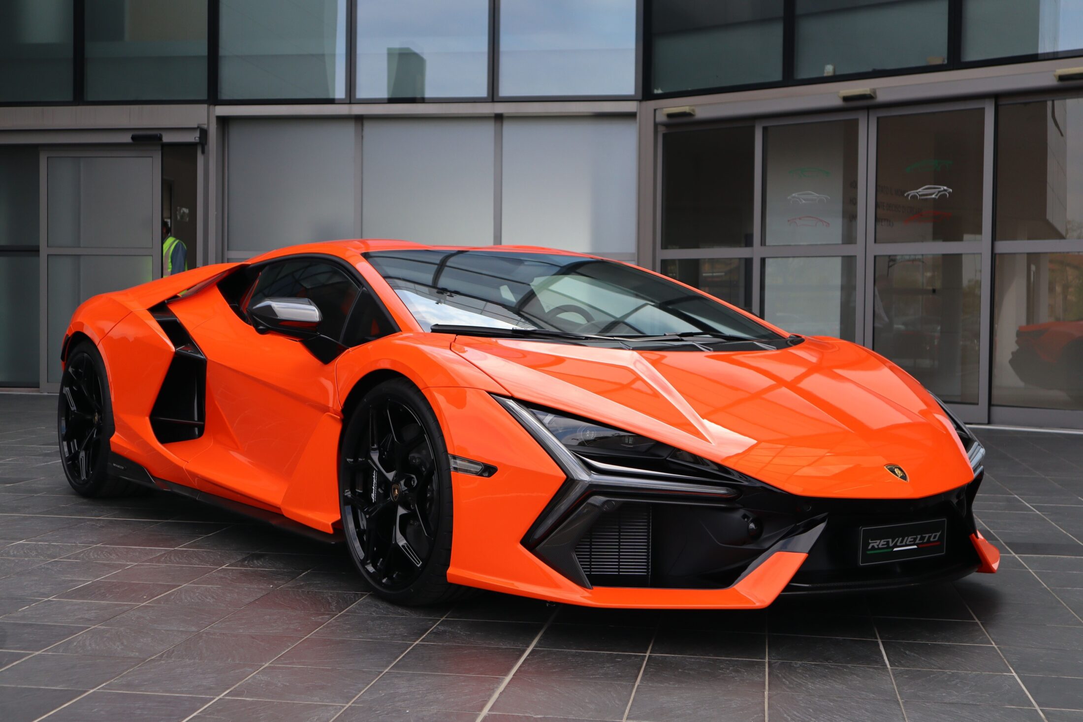 Lamborghini Revuelto orange devant un bâtiment vitré